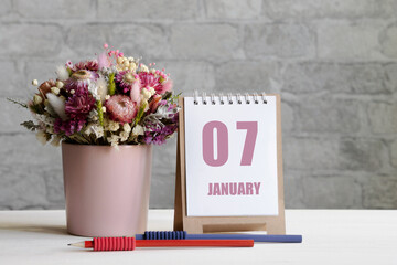 january 07. 07-th day of the month, calendar date.A delicate bouquet of flowers in a pink vase, two pencils and a calendar with a date for the day on a wooden surface