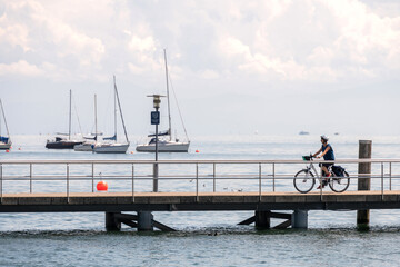 Naturerlebnis am Bodensee mit dem Fahrrad, Frau fährt mit Elektro Fahrrad auf Bootssteg, weiter...