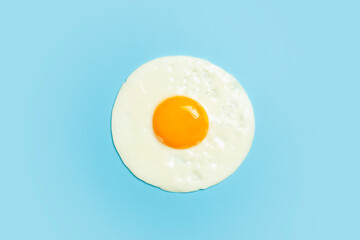 Fried egg is minimal. Fried egg isolate on a blank color light blue background. Creative breakfast and food idea.