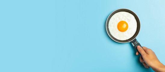 Fried egg is minimal. Fried egg in a frying pan on an empty blue banner background. Creative breakfast and food idea.