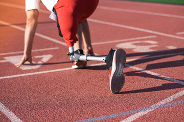Caucasian male athlete with a prosthetic leg standing at the start on the track at the stadium. Back view. Sport concept.