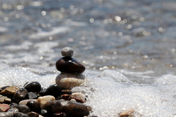 Pyramid of wet pebbles in foaming sea waves. Summer vacation, beach stones, balance and relax concept