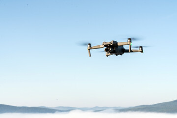Fototapeta na wymiar drone quadcopter helicopter in the air, in a clear blue sky, morning fog and mountains below. aerial photo and video shooting using gadgets and modern devices