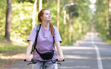 Naklejka premium Redhead girl rides a bicycle in a beautiful summer forest. Young woman travels by bike.