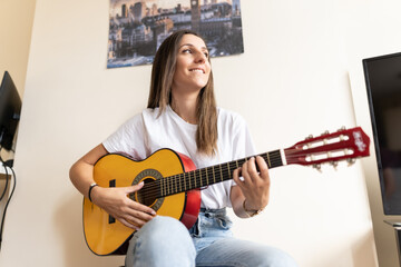 Attractive young female playing the guitar at home while learning new chords and practising new...