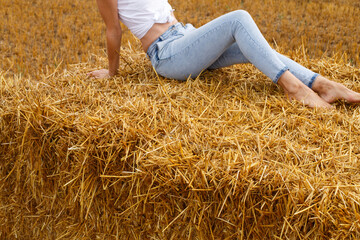 girl sitting on a haystack on a bale in the agricultural field after harvesting