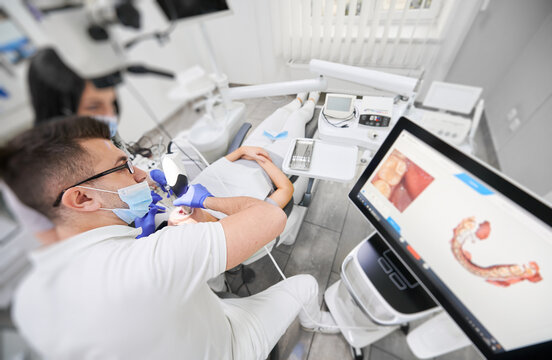 Dentist and assistant in medical masks using dental intraoral scanner while examining patient teeth in dental office. Intraoral scanning with modern scanning machine. Concept of digital dentistry.