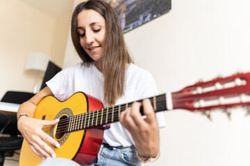 Fototapeta premium Attractive young female playing the guitar at home while learning new chords and practising new songs