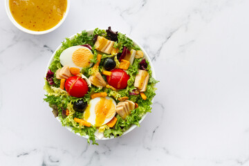 Salad with lettuce, egg, tuna, olives and honey and mustard vinaigrette on white background