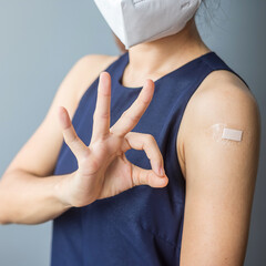 Happy woman showing OK sign with bandage after receiving covid 19 vaccine. Vaccination, herd immunity, side effect, efficiency, vaccine passport and Coronavirus pandemic