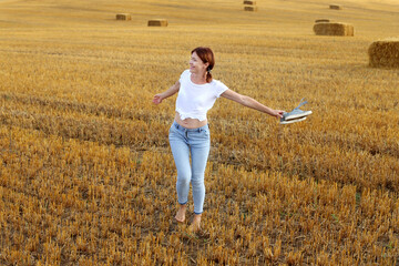 barefoot girl with sneakers in hand walking in the agricultural field with haystack and bales