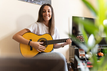 Attractive young female searching on the internet for tutorials to learn at home new chords and how...