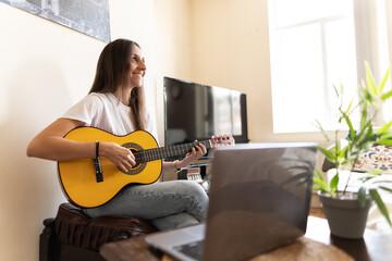 Attractive young female searching on the internet for tutorials to learn at home new chords and how to play the guitar
