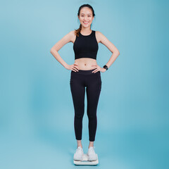 Portrait of beautiful asian fitness woman standing on weight scale after exercise with happy face on blue colour background.Concept of slim and healthy workout.