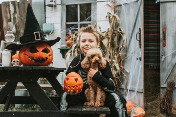 boy in a skeleton costume with a dog on the porch of a house decorated to celebrate a Halloween...