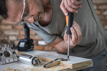 A man is screwing in a screw, a self-tapping screw for wood.