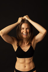 Portrait of young beautiful slim tanned woman in black lingerie posing isolated over dark studio background. Natural beauty, wellness, healthy lifestyle concept.