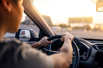 Close-up - Hand of man driving car along the highway, the setting sun shines in the windshield....