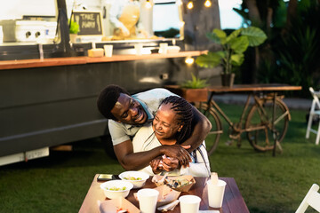 Happy Afro mother and son having fun eating in a street food truck market outdoor