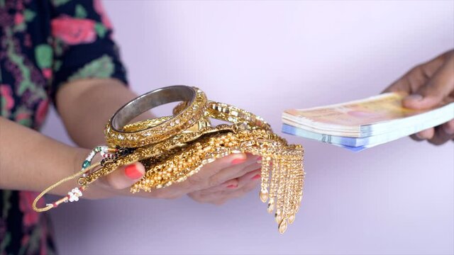 Young woman in casual clothes mortgaging her gold jewelry for cash - gold loan. Lady with a bundle of Indian currency notes 