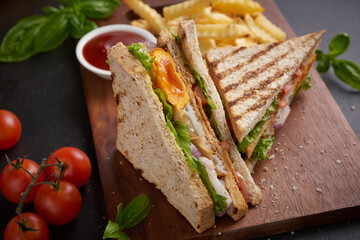 Club-sandwich with french fries. Sandwich with bacon, fried egg. Grilled and pressed toast with bacon, fried egg, tomato and lettuce served on wooden cutting board.