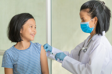 Asian little girl in doctor's office is vaccinated. Syringe with vaccine for covid-19...