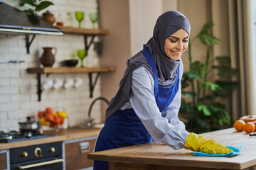 Joyful Muslim woman cleaning a table in the kitchen
