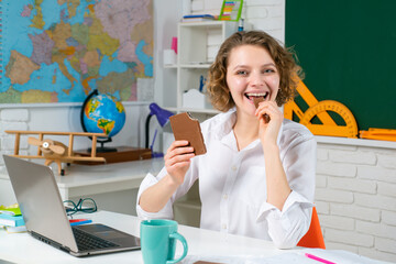 Portrait of smiling female teacher eat chocolate near blackboard in classroom at school.