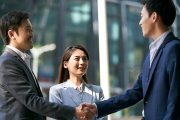 asian business people shaking hands outdoors on downtown street in modern city