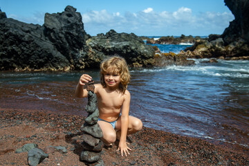 Fototapeta na wymiar Kid making pebbles are piled on a volcanic rock by the sea. Zen concept.