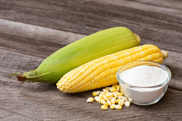 Corn starch in wooden bowl and fresh sweetcorn with kernels on wood table background. 