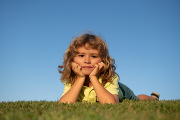 Portraits of happy kids playing and laying on grass outdoors in summer park. Funny child face outdoor.