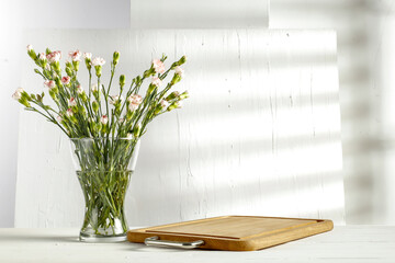 Flowers in a vase against a white wall and shadows of bright morning sun on a holiday day 