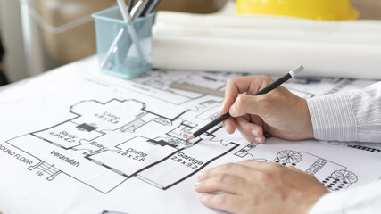 Architectural building design and construction plans with blueprints, Young man was designing a building or architecture with a pen ruler, pencil, tape measure, architect hat and other equipment.