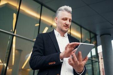 A lawyer prepares a presentation before a meeting with colleagues. The manager is holding a tablet and prints a message to the client's email. The entrepreneur is a gray-haired man in a business suit.