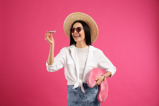 Happy female tourist with toy plane and travel pillow on pink background