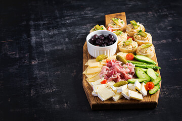 Antipasto catering platter with jamon, cheese, canape and black olives on a wooden board. Top view,...
