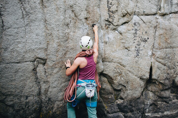Young woman wearing in climbing equipment standing in front of a stone rock outdoor and preparing...
