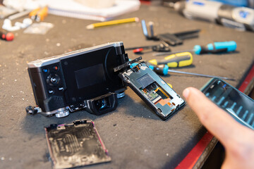 Close-up of disassembled camera and hands of man consulting technical data with mobile phone in the technical service.
