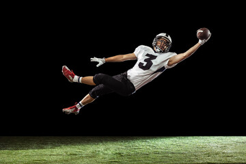 Portrait of American football player training isolated on dark studio background with green grass...