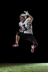 Fototapeta na wymiar Portrait of American football player training isolated on dark studio background with grass flooring. Concept of sport, competition, goals, achievements