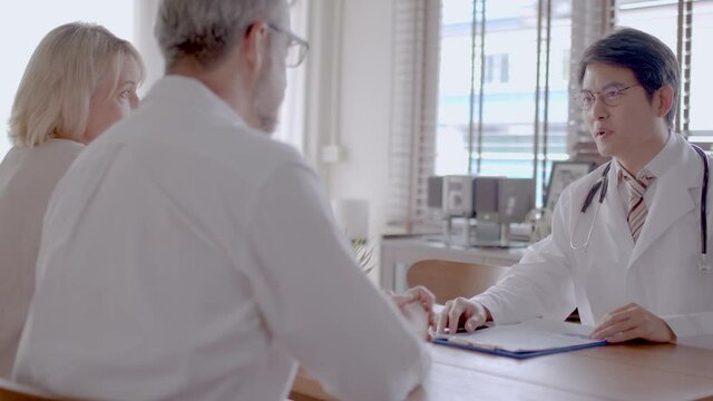 Senior Caucasian couple consult with young Asian doctor. medium close-up with slide movement.  
