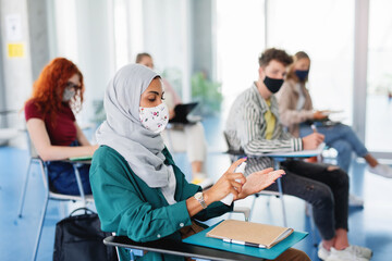 University students disinfecting hands in classroom indoors, coronavirus and back to normal concept.