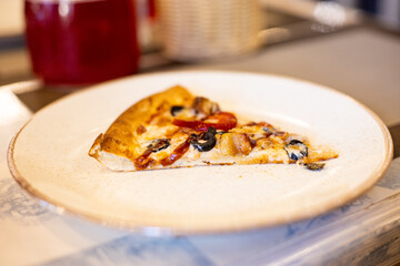 Slice of pizza on white plate on the table of restaurant