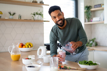 Young man preparing healthy breakfast indoors at home, looking at camera.