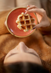 food, season and leisure concept - close up of woman eating waffle at home