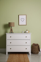 Modern white chest of drawers with lamp and decor near light green wall indoors