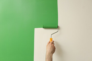 Man applying green paint with roller brush on white wall, closeup