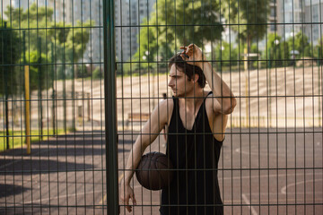 Side view of sportsman with basketball ball standing near fence of playground