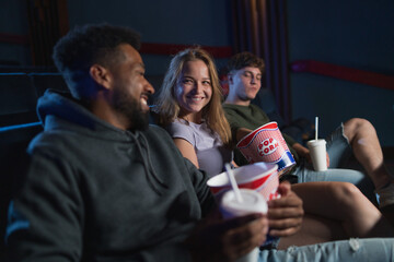 Cheerful young couple with popcorn in the cinema, talking.